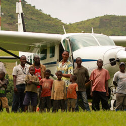 Group of children and men in front of plane mountains in background